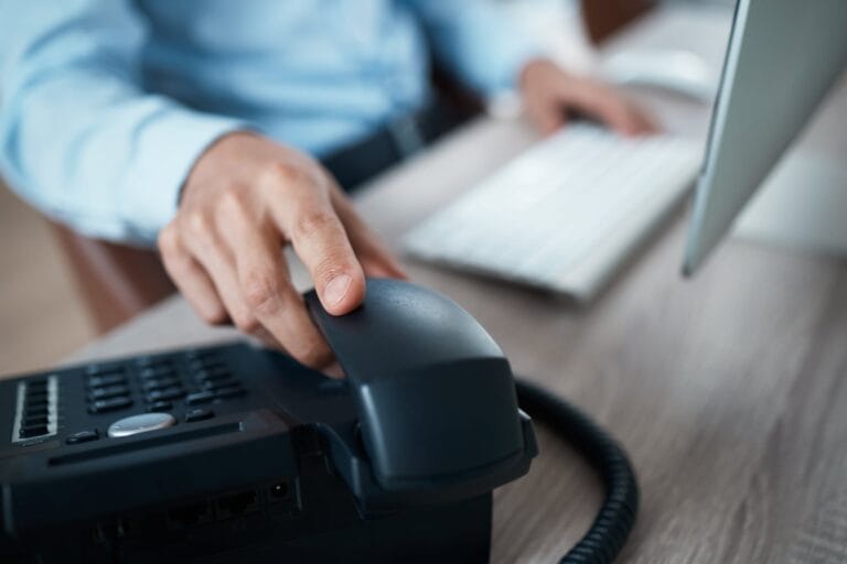 Ein Ingenieur sitzt am Computer und greift zum Telefonhörer, um ein Beratungsgespräch einzuleiten.