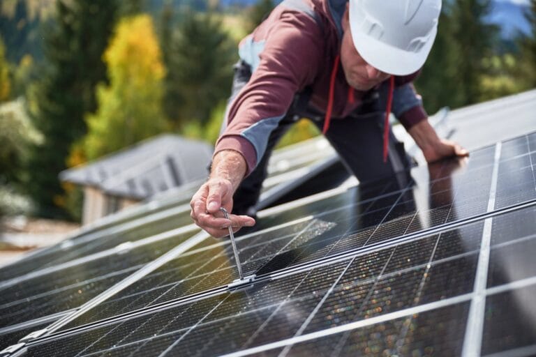 Ein Arbeiter installiert Solarmodule einer PV-Anlage auf dem Dach eines Einfamilienhauses.