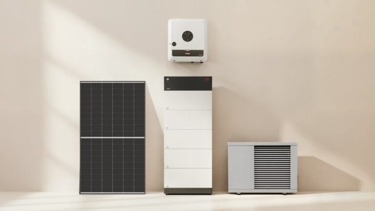 Ein Solarmodul sowie ein Hybridwechselrichter einer PV-Anlage, ein weißer Batteriespeicher und eine Wärmepumpe stehen vor einer schlichten, hellen Wand in einem sonnenbeschienenen Raum.