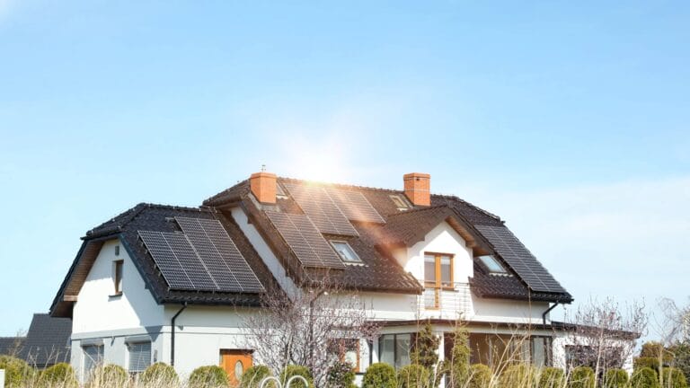 Ein modernes Haus mit einer PV-Anlage, auf deren Dach mehrere Solarmodule installiert sind, sonnt sich unter einem strahlend blauen Himmel mit Sonnenschein.